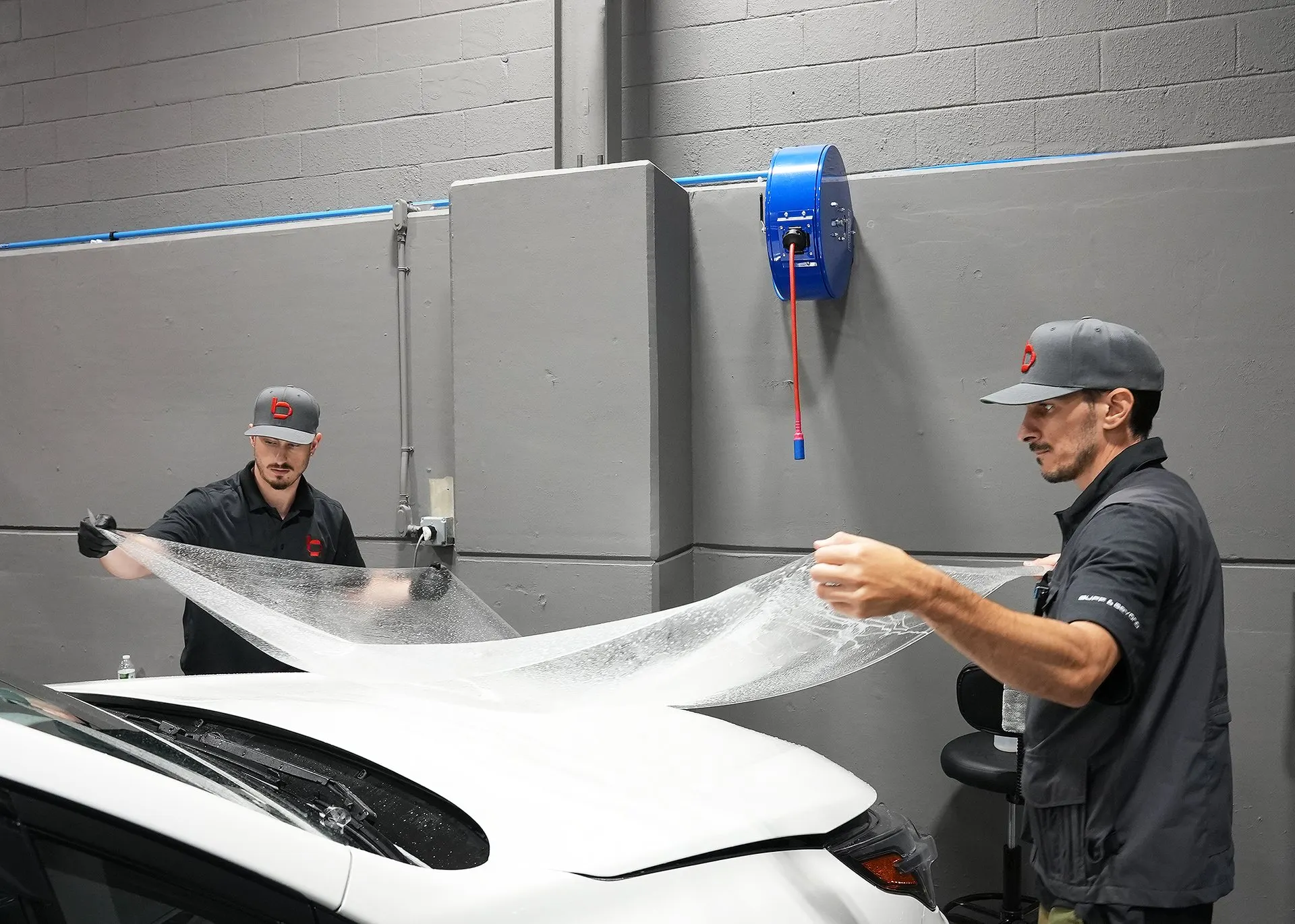 Two installers laying film over a hood